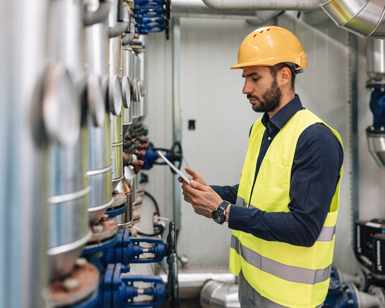 Person in Warnweste und mit Tablet in der Hand prüft Maschinen