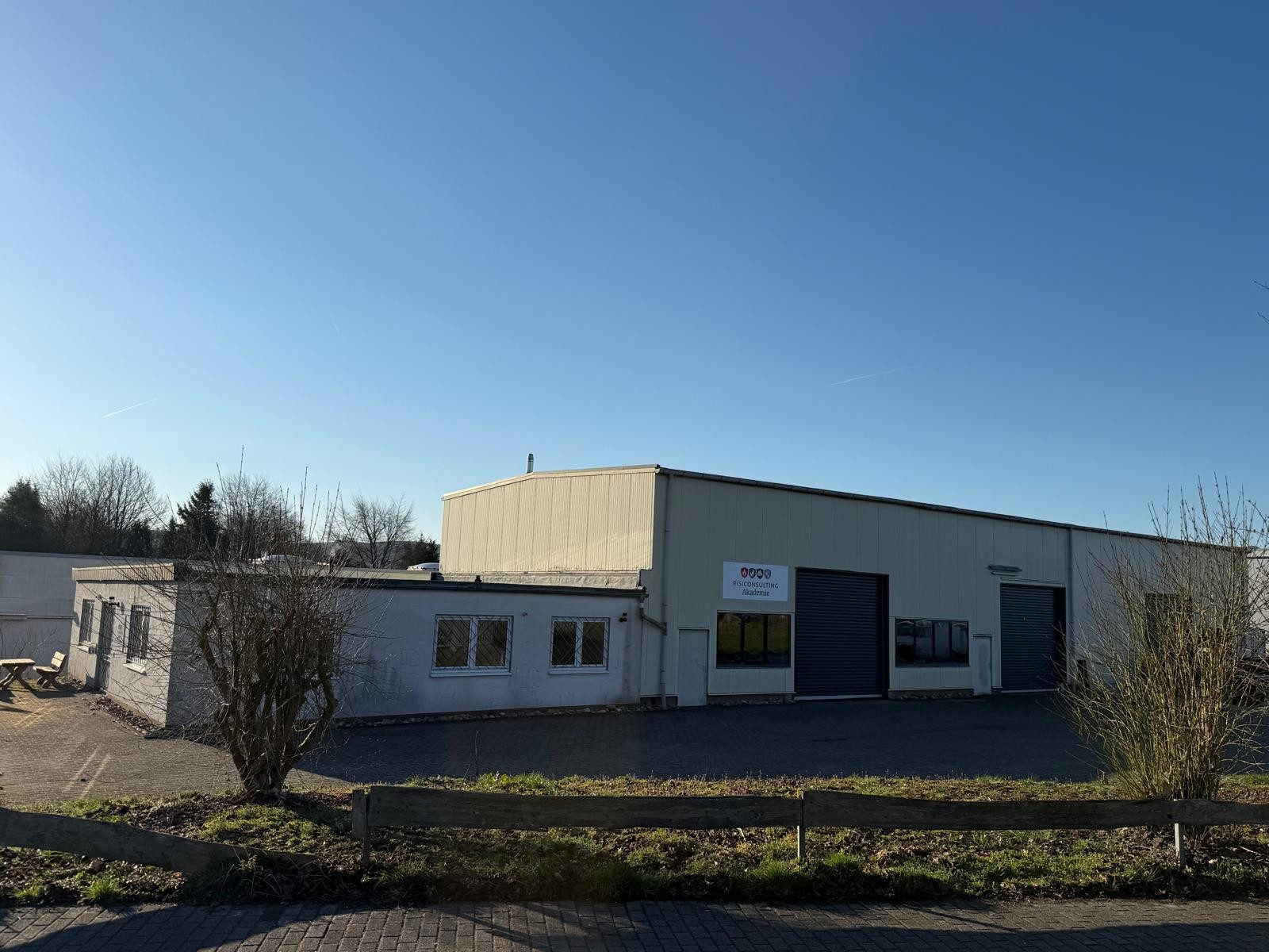 Aussenansicht der RISICONSULTING Akademie mit Parkplatz und Pausenbereich bei Sonnenschein